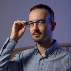 Portrait of a person in a blue shirt adjusting glasses, dramatic side light.